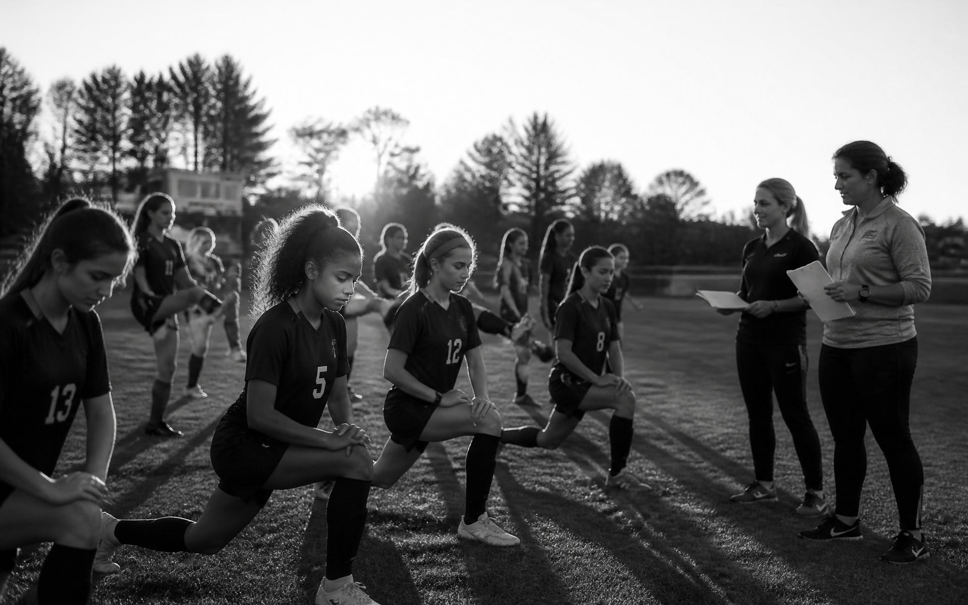 Female high school soccer team warming up together with their coach and athletic trainer nearby